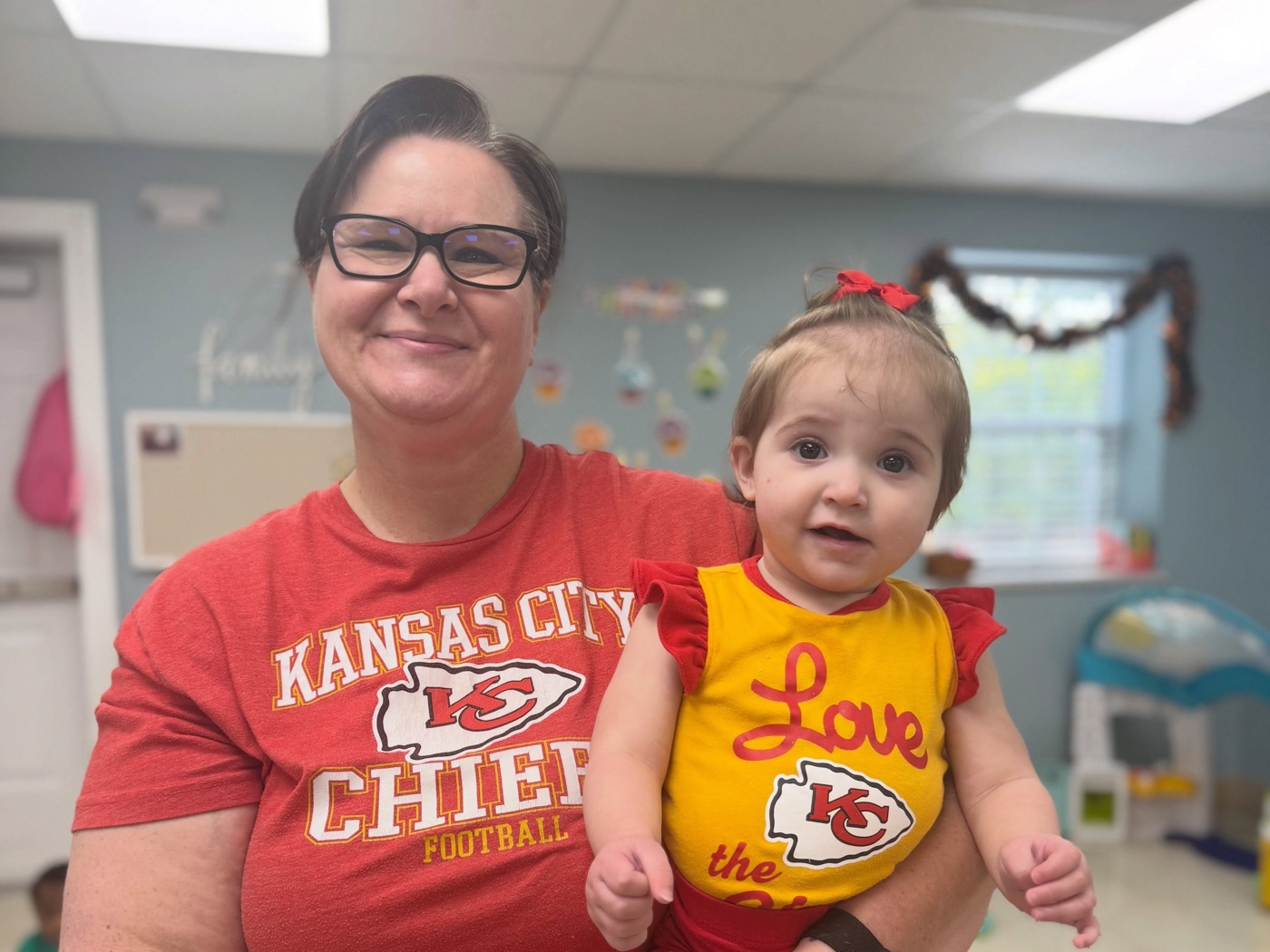 A caring teacher holding a happy baby in the Bright Skies infant room