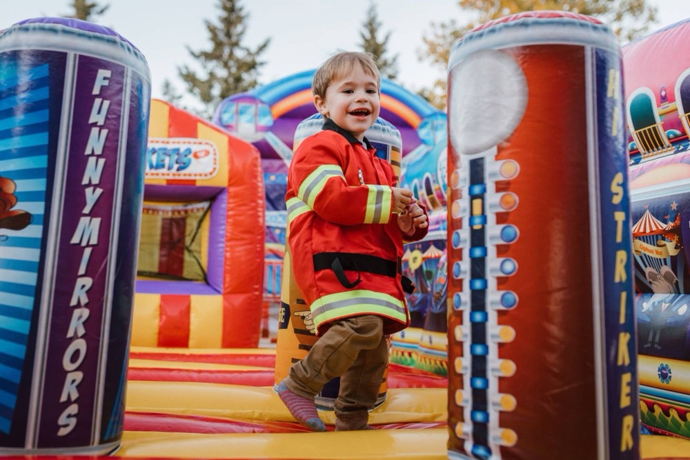 A child in a firefighter costume beaming on the bounce house at a past Trunk or Treat